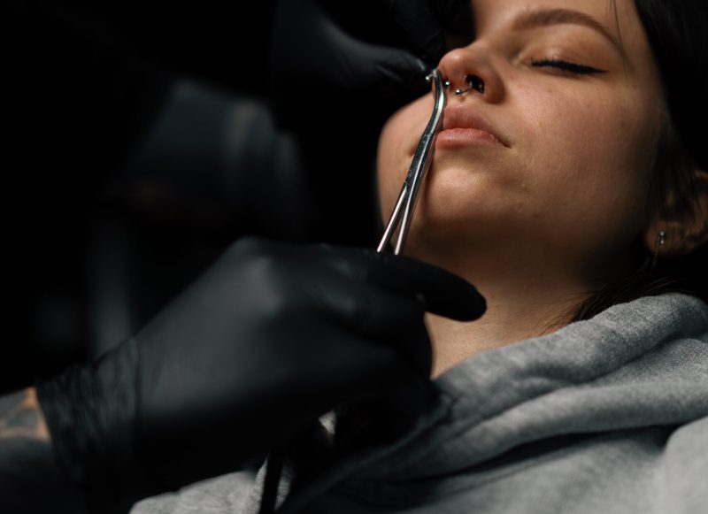 Piercing process Professional nose piercing of girl in disposable black gloves sexy nose ring